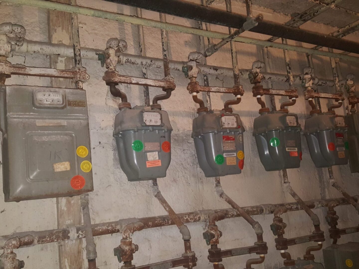 Rusty gas meters and pipes on wall.