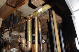 Old plumbing pipes in a wooden ceiling.