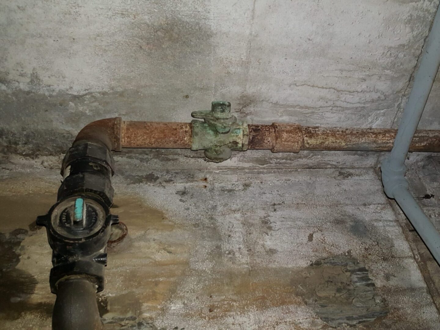 Rusty pipes and valve in concrete wall.