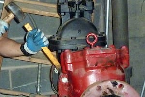 Worker hammering a large industrial valve.